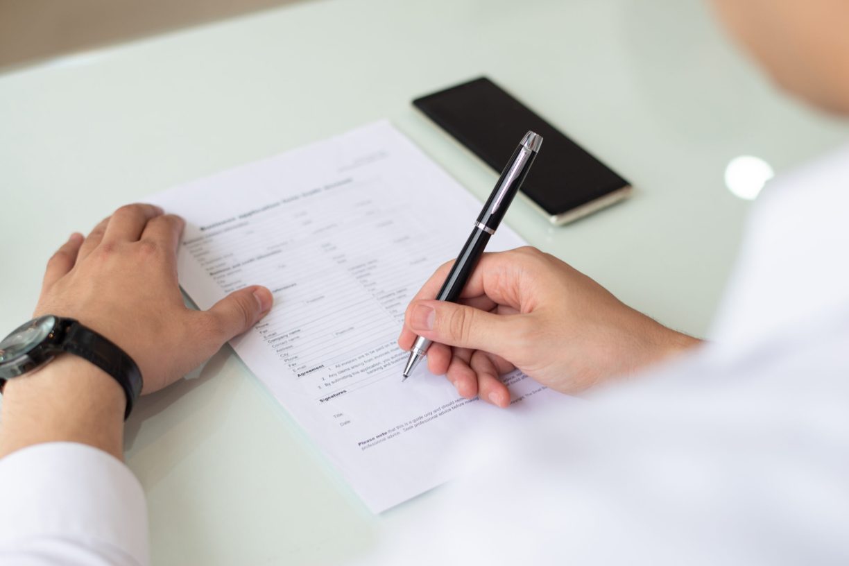 Hands of businessman or student filling application form. Close-up of young Caucasian man sitting at table and signing document. Job search concept