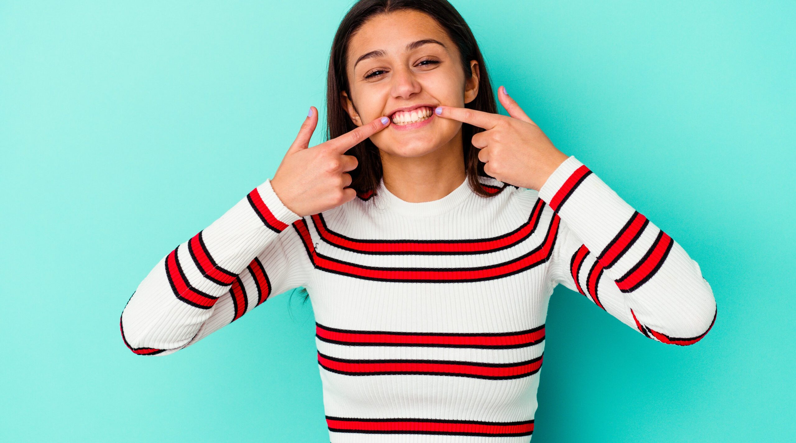 Young Indian woman isolated on blue background smiles, pointing fingers at mouth.